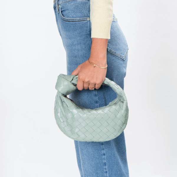 Frau trägt eine pastellgrüne Ledertasche der Marke Bottega Veneta mit Knotendesign im Griff.
