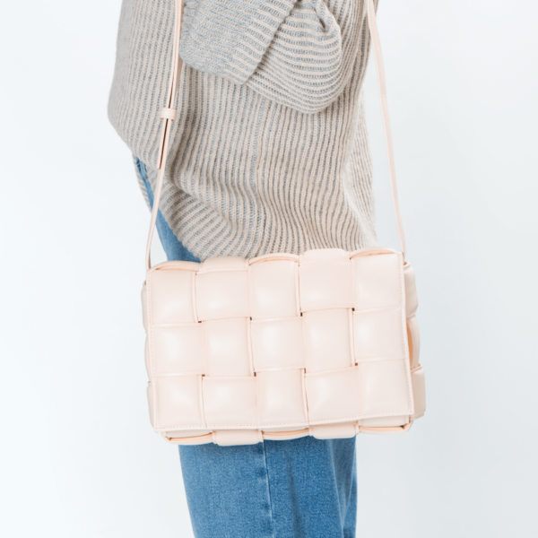 Frau trägt eine Lederhandtasche im Flechtmuster und hellem Pfirsichton der Marke Bottega Veneta.