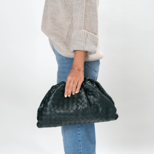 Frau trägt eine dunkelgrüne Clutch-Tasche der Marke Bottega Veneta im Webmuster Design.