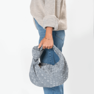 Frau trägt eine graue Veloursledertasche der Marke Bottega Veneta mit Knotendesign im Griff.