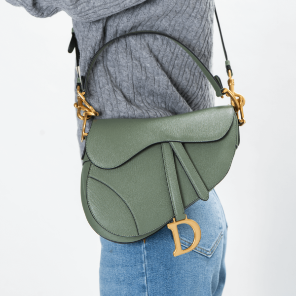 Frau trägt eine grüne Handtasche mit goldener Hardware der Marke Dior.