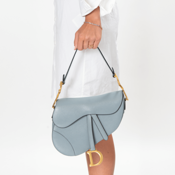 Frau trägt eine hellblaue Handtasche mit goldener Hardware der Marke Dior.