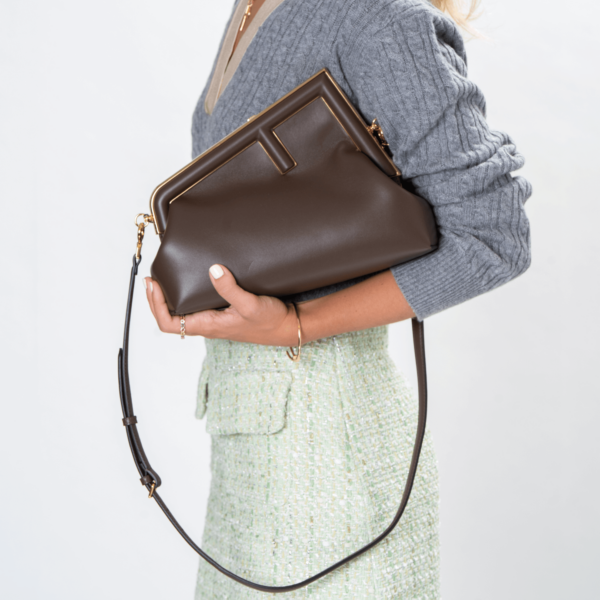 Frau trägt eine braune Clutch-Tasche mit goldener Hardware der Marke Fendi.