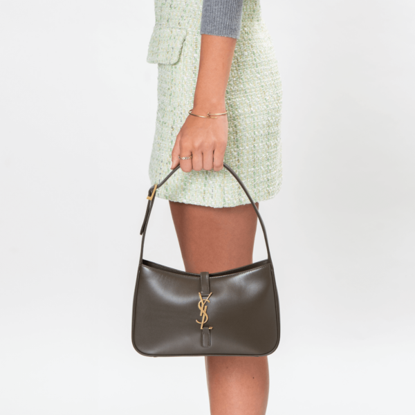 Frau trägt eine kleine Schultertasche aus braunem Leder und goldener Hardware der Marke Saint Laurent.